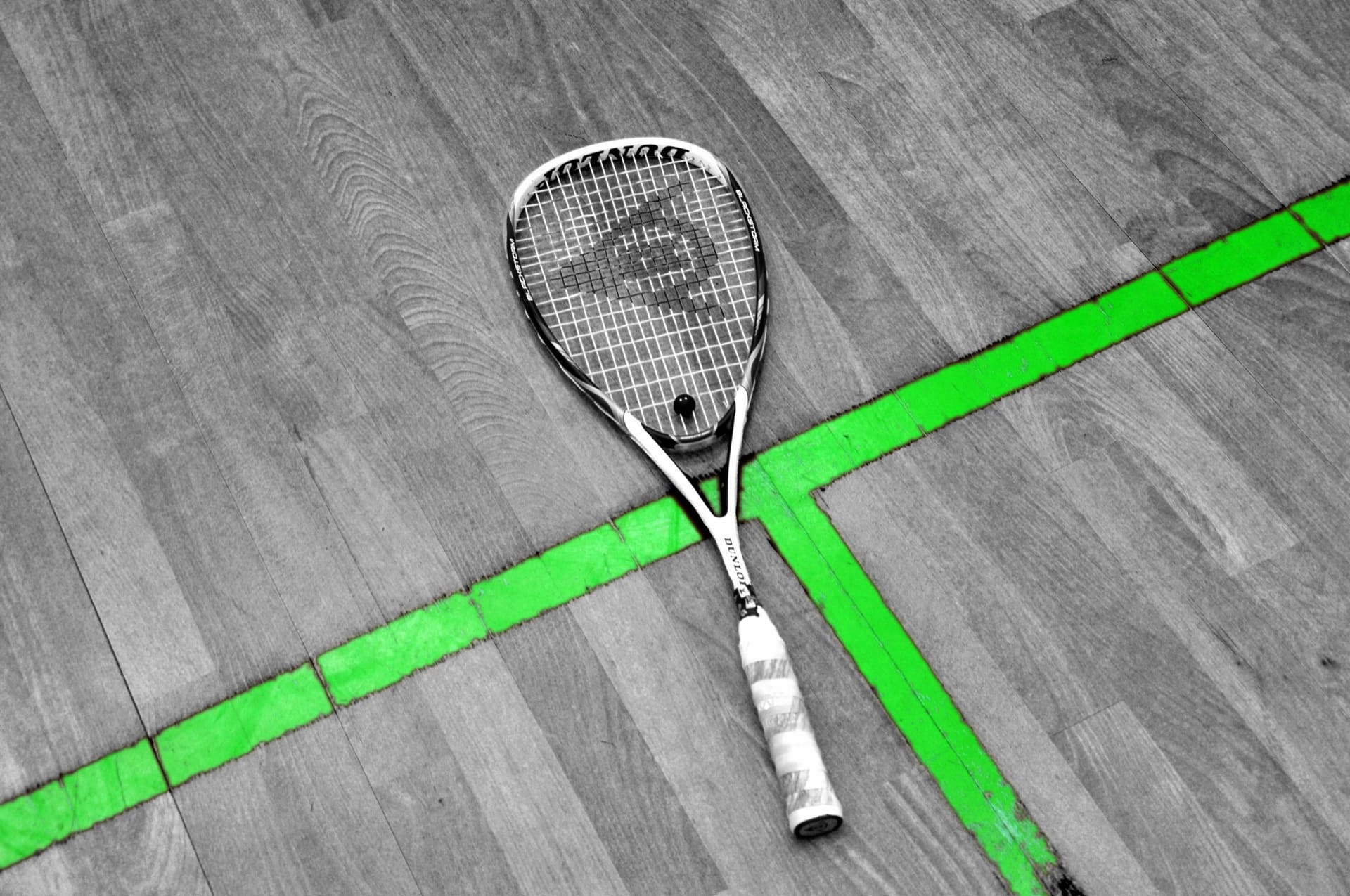 Squashschläger auf dem Parkett eines Courts, darunter das grüne T der Bodenlinien